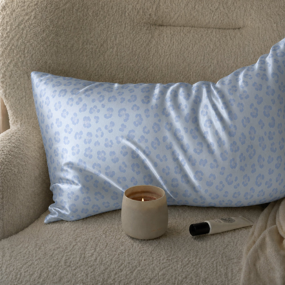 Blue Leopard 22 momme silk front pillowcase styled on a cream lounge chair beside a candle.
