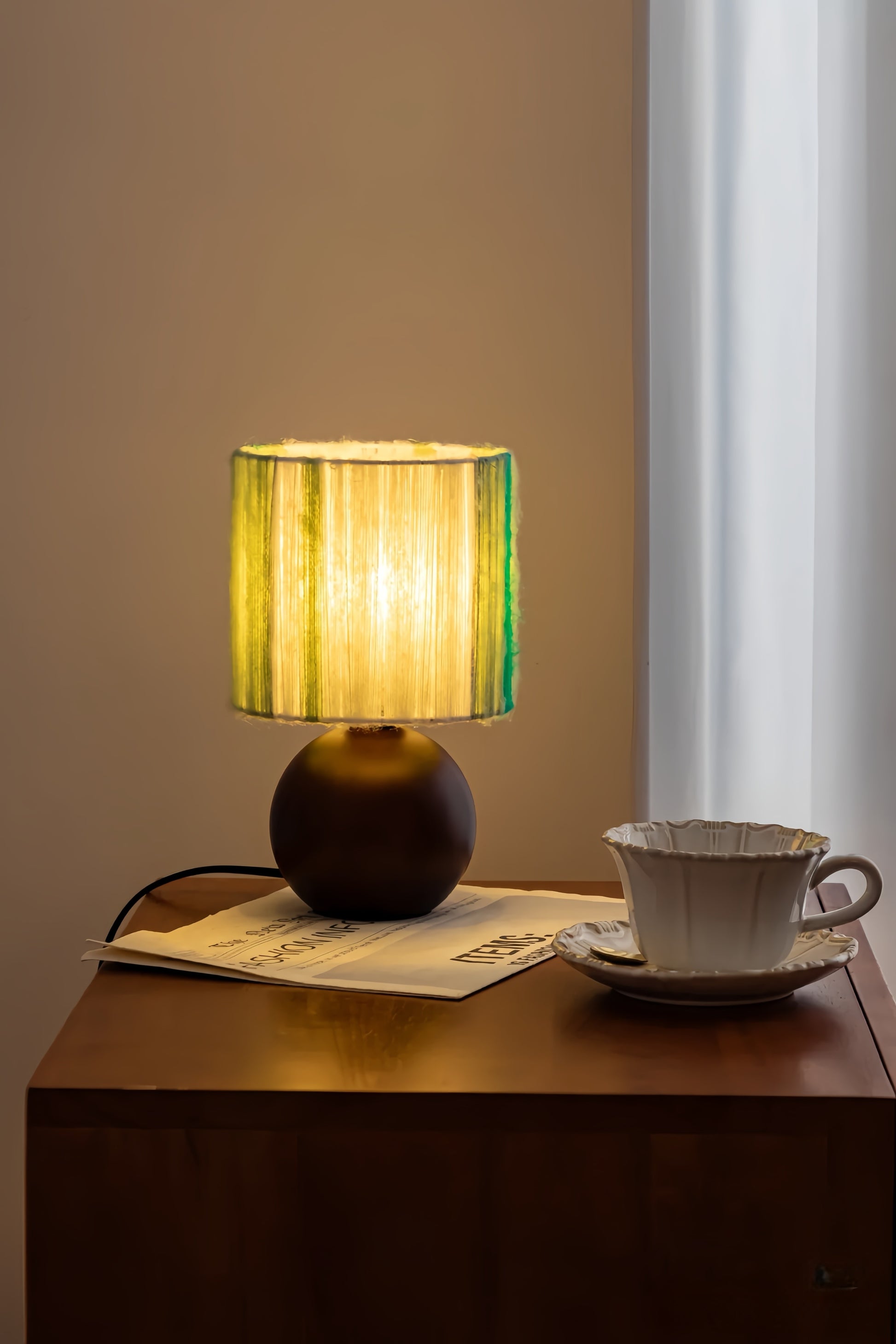 MCM table lamp with a green shade on a wooden surface next to a teacup and saucer.