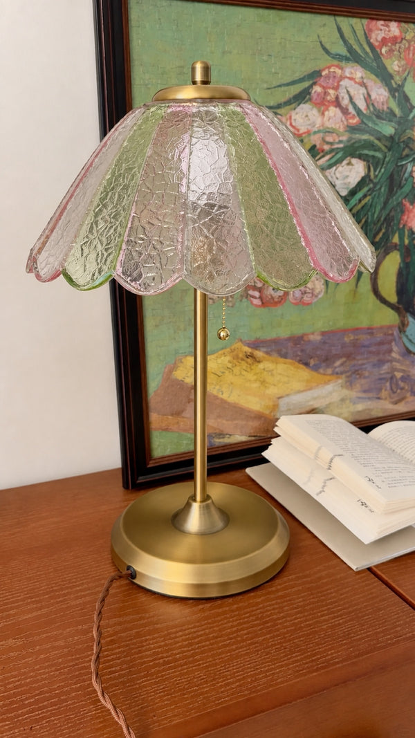 The water-ripple glass catches daylight and gives the pink, green, and clear panels visible depth. Styled beside books and colorful art, the lamp reads as a decorative object rather than simply a source of light.