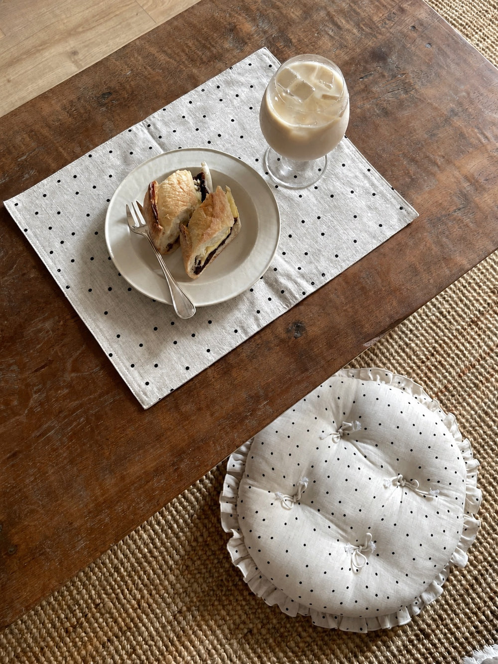 Overhead lifestyle view of a cream polka dot round chair cushion with bow ties and a ruffled edge next to a wooden coffee table.