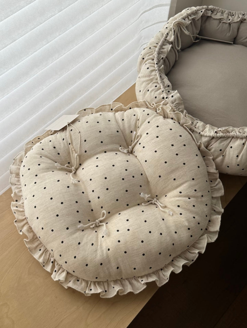 Cream polka dot round chair cushion with bow ties and a ruffled edge viewed from above, showing the linen-blend texture.