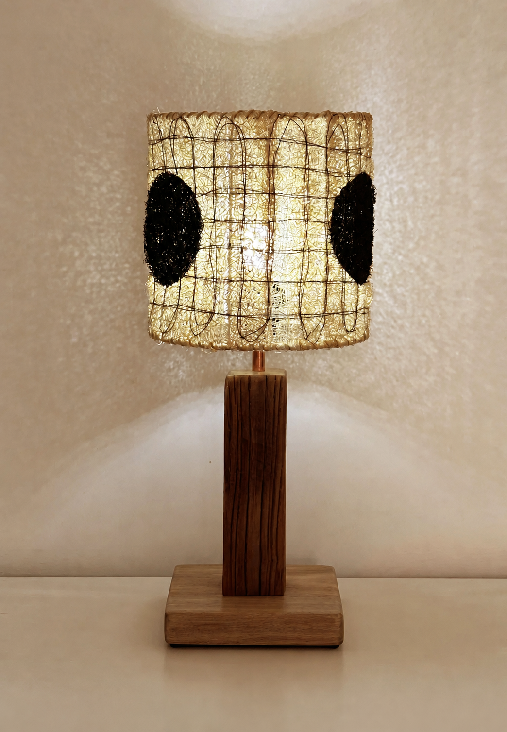 Dottie black dot loofah table lamp illuminated with a warm patterned glow against a wall