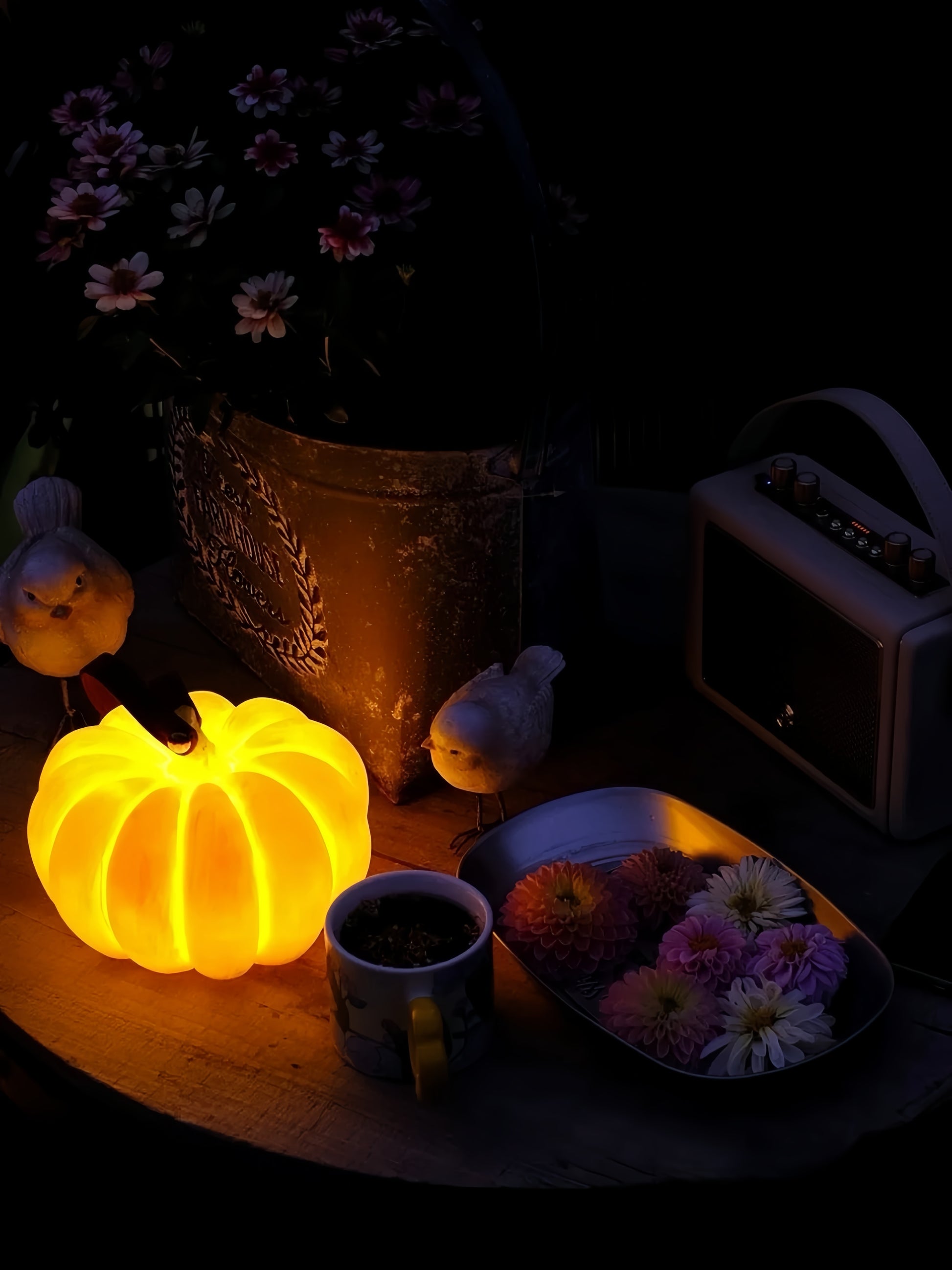 Glowing pumpkin-shaped light on a table with flowers and a radio in the dark