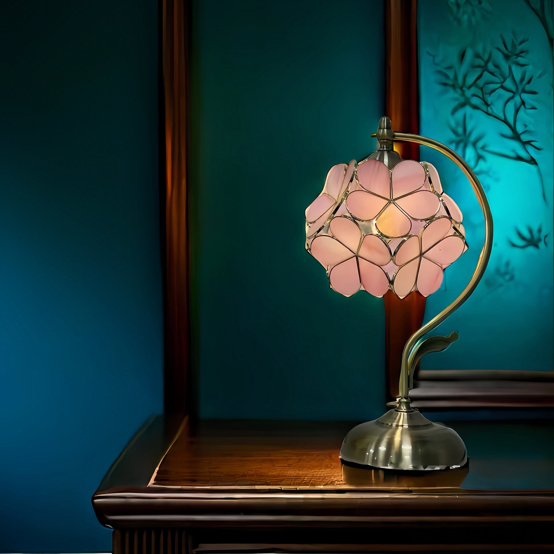 French vintage table lamp with pink floral glass shade on a wooden surface against a teal wall.