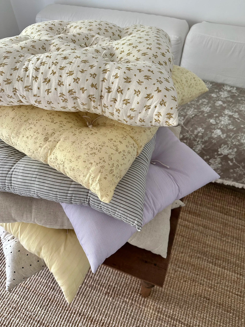 Assorted French vintage patterned pillow cushions stacked on a bed in a cozy bedroom.