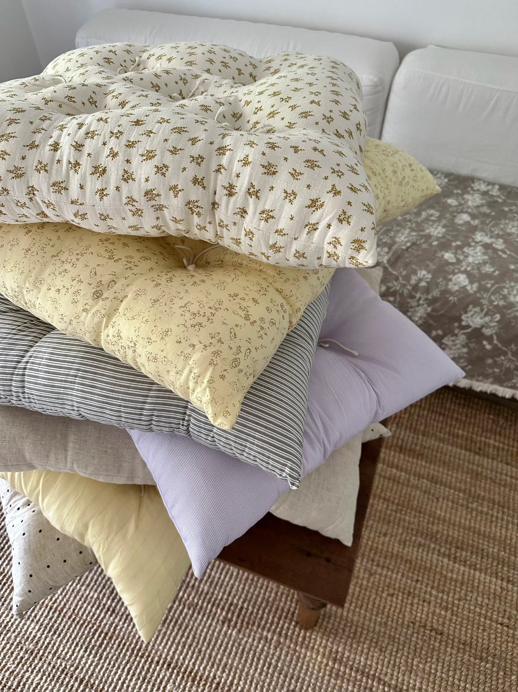 Assorted French vintage patterned pillow cushions stacked on a bed in a cozy bedroom.