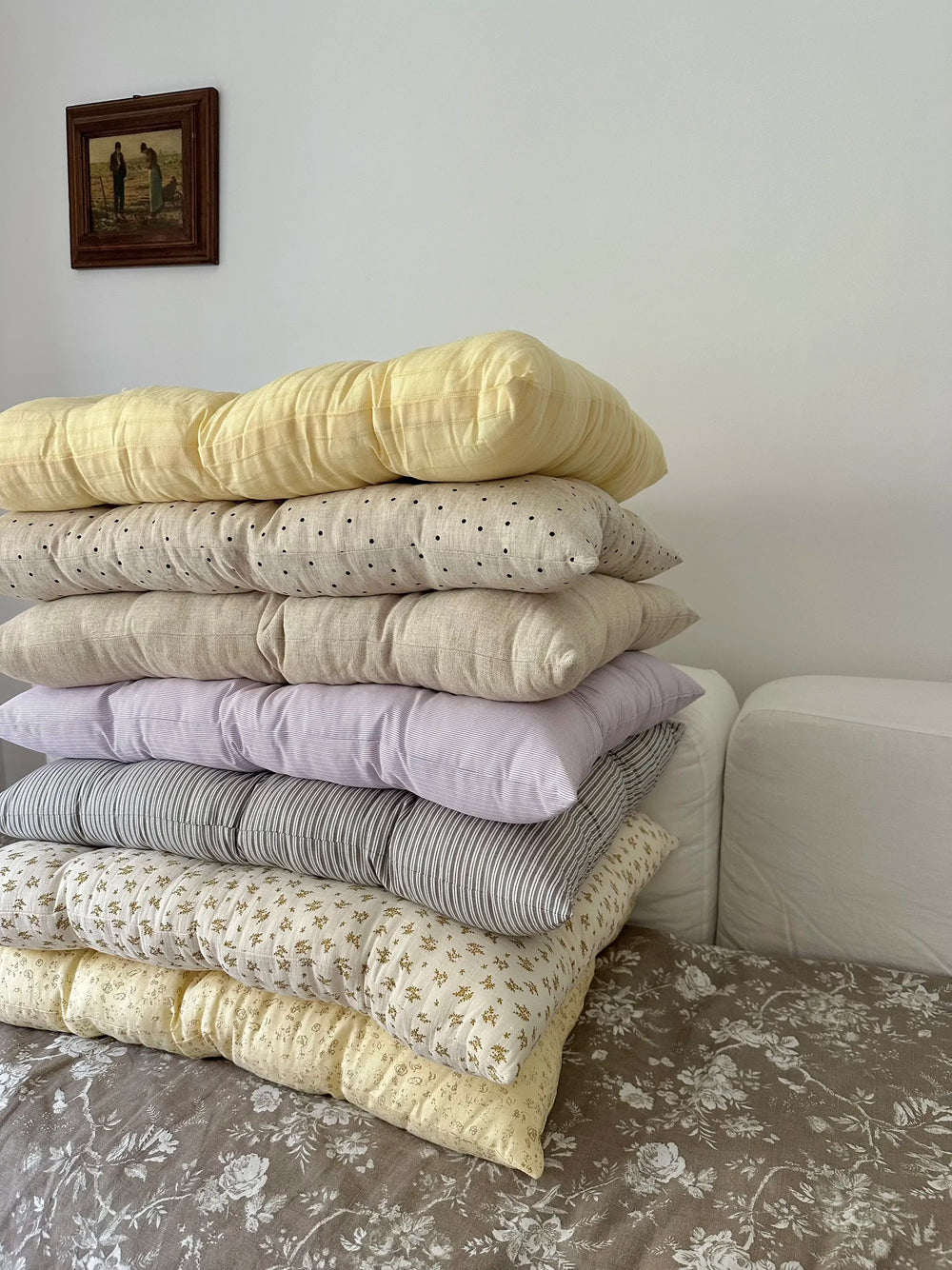 Mixed color French vintage patterned pillow cushions stacked against a sofa in a soft bedroom scene.