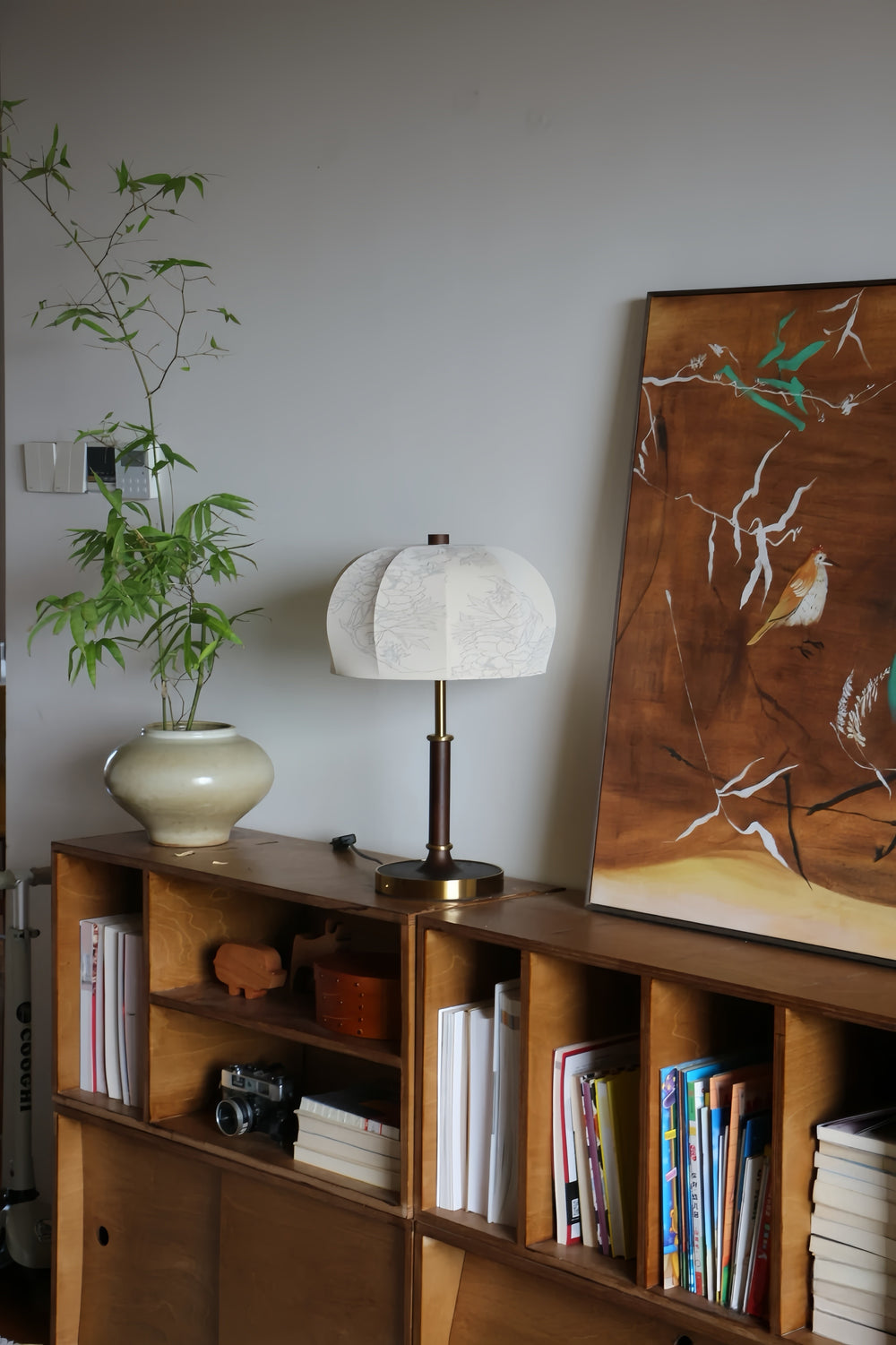Wooden shelf with books, a french vintage lamp, and a plant against a white wall.