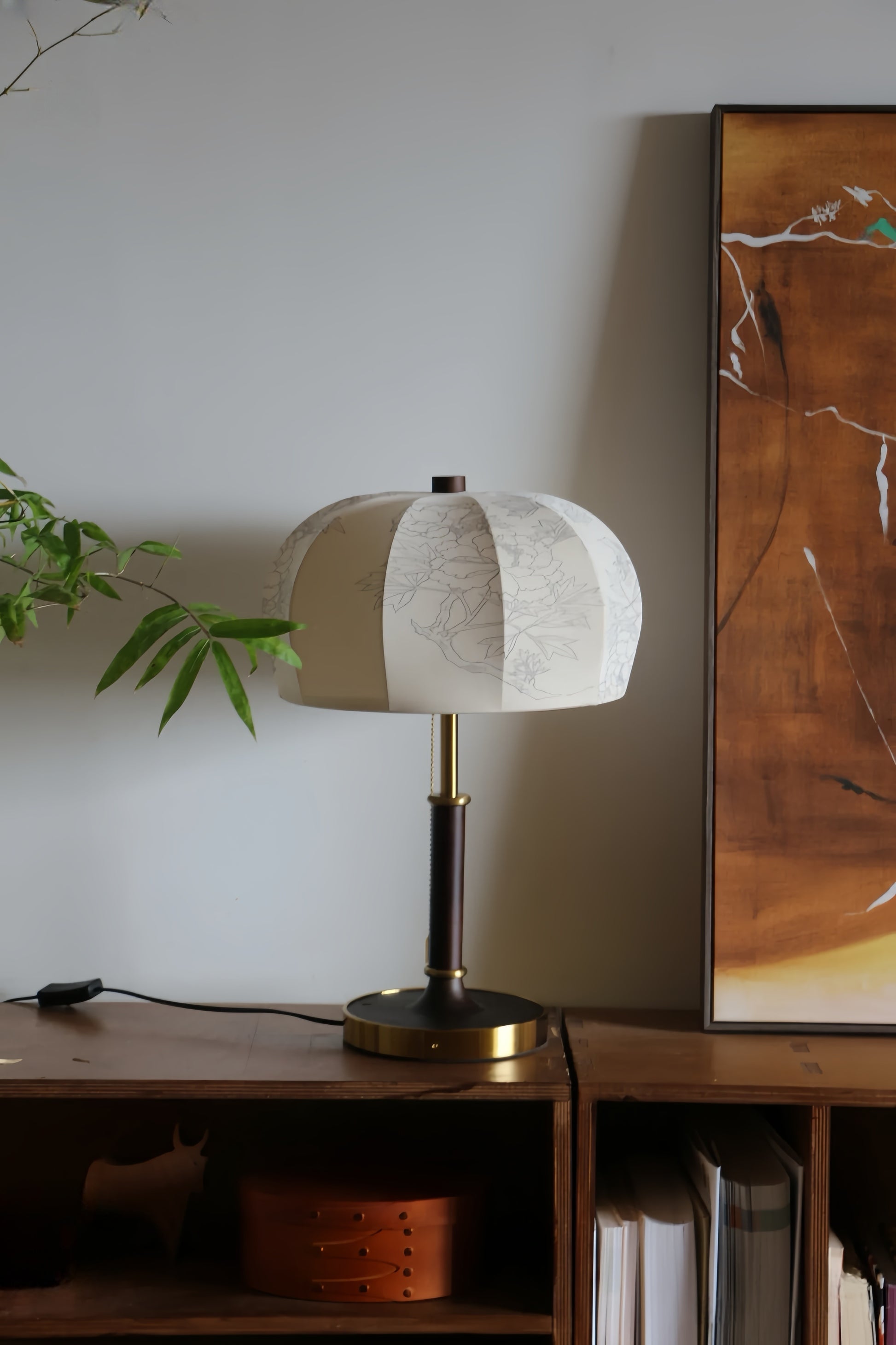 French vintage table lamp on a wooden surface with a plant and abstract painting in the background