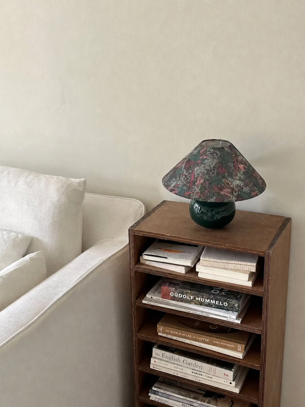 Beside a sofa and stacked books, the lamp adds pattern and character to a compact reading corner while leaving the narrow shelf useful for everyday storage.