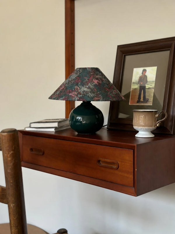 Among framed photographs, books, and dark wood, the lamp feels naturally at home with personal objects collected over time.