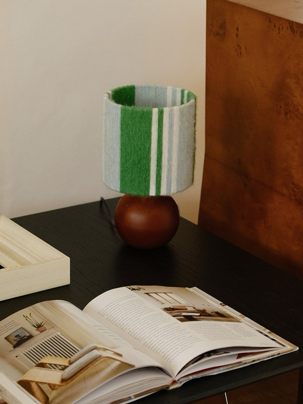 Sage & Forest Mohair & Oak Wood Table Lamp - Verdino overhead shot on a dark desk with magazine showing the green-white striped mohair drum shade