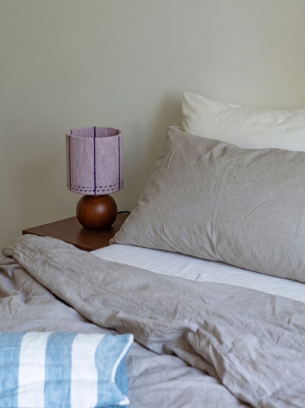Dusty Lavender Mohair & Oak Wood Table Lamp on a wooden nightstand beside bed showcasing the lavender stitched cylinder shade