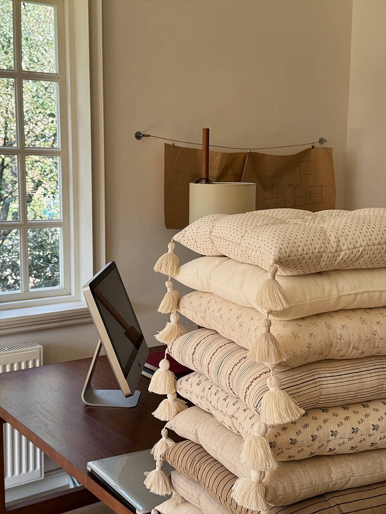 Neutral patterned Mariette tufted tassel throw pillows stacked beside a window and desk.