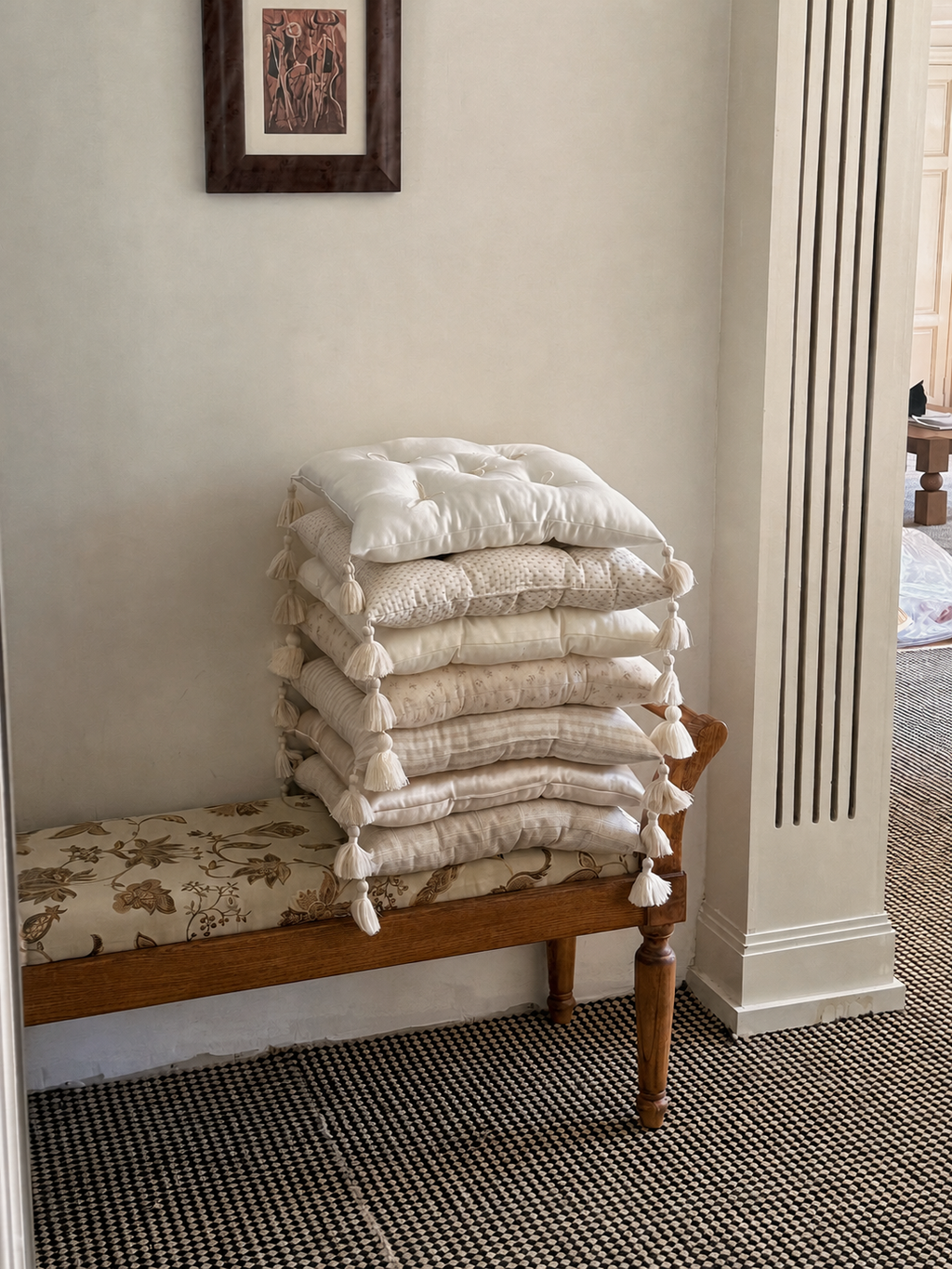 A stack of neutral Mariette tufted tassel throw pillows displayed on a wooden bench.