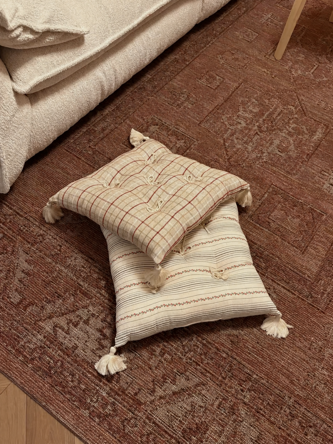 Red plaid and floral stripe Mariette tufted tassel throw pillows styled on a patterned rug.