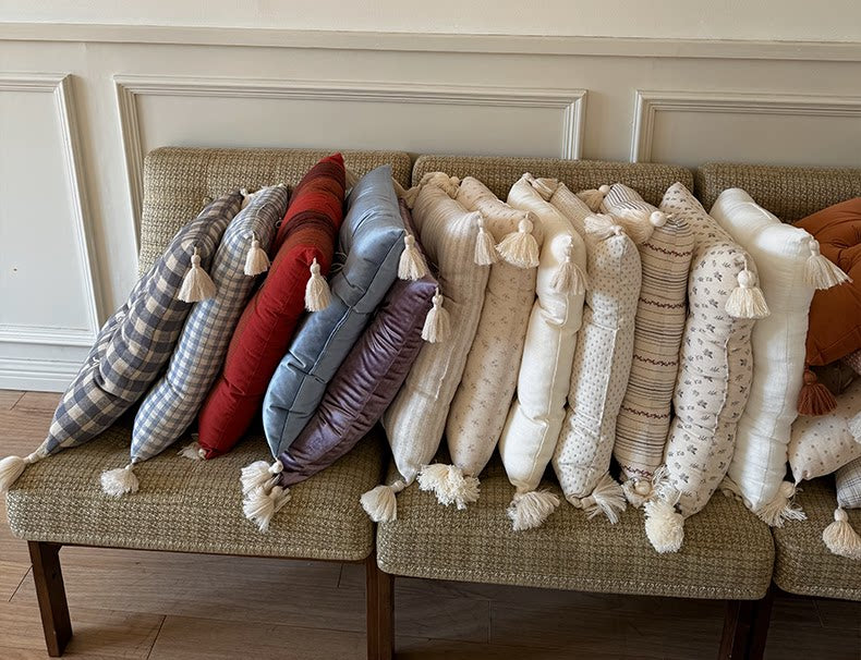 Assorted Mariette tufted tassel throw pillows lined up across a vintage sofa.