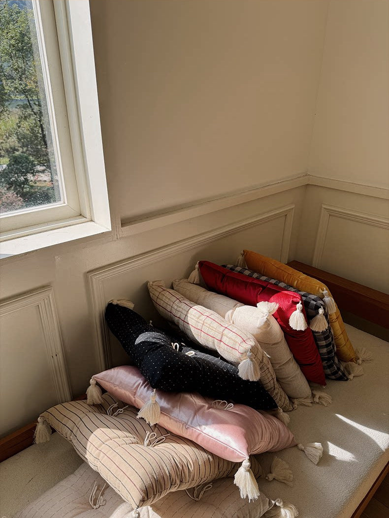 A colorful pile of Mariette tufted tassel throw pillows styled on a sunlit window bench.