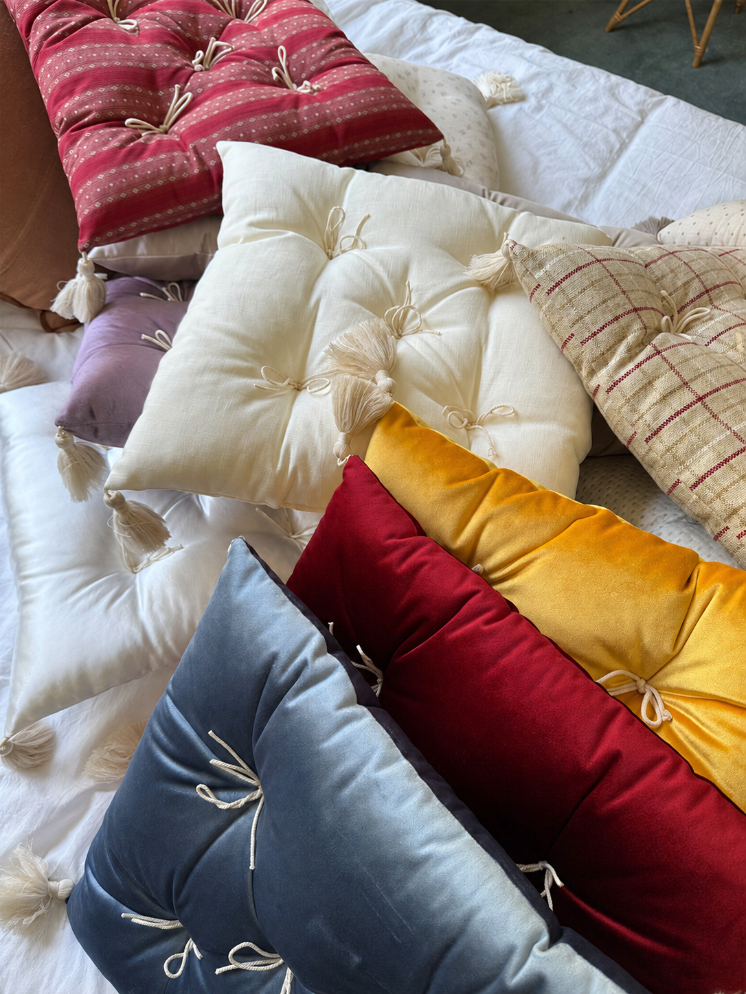 A layered collection of Mariette tufted tassel throw pillows arranged on a bed.