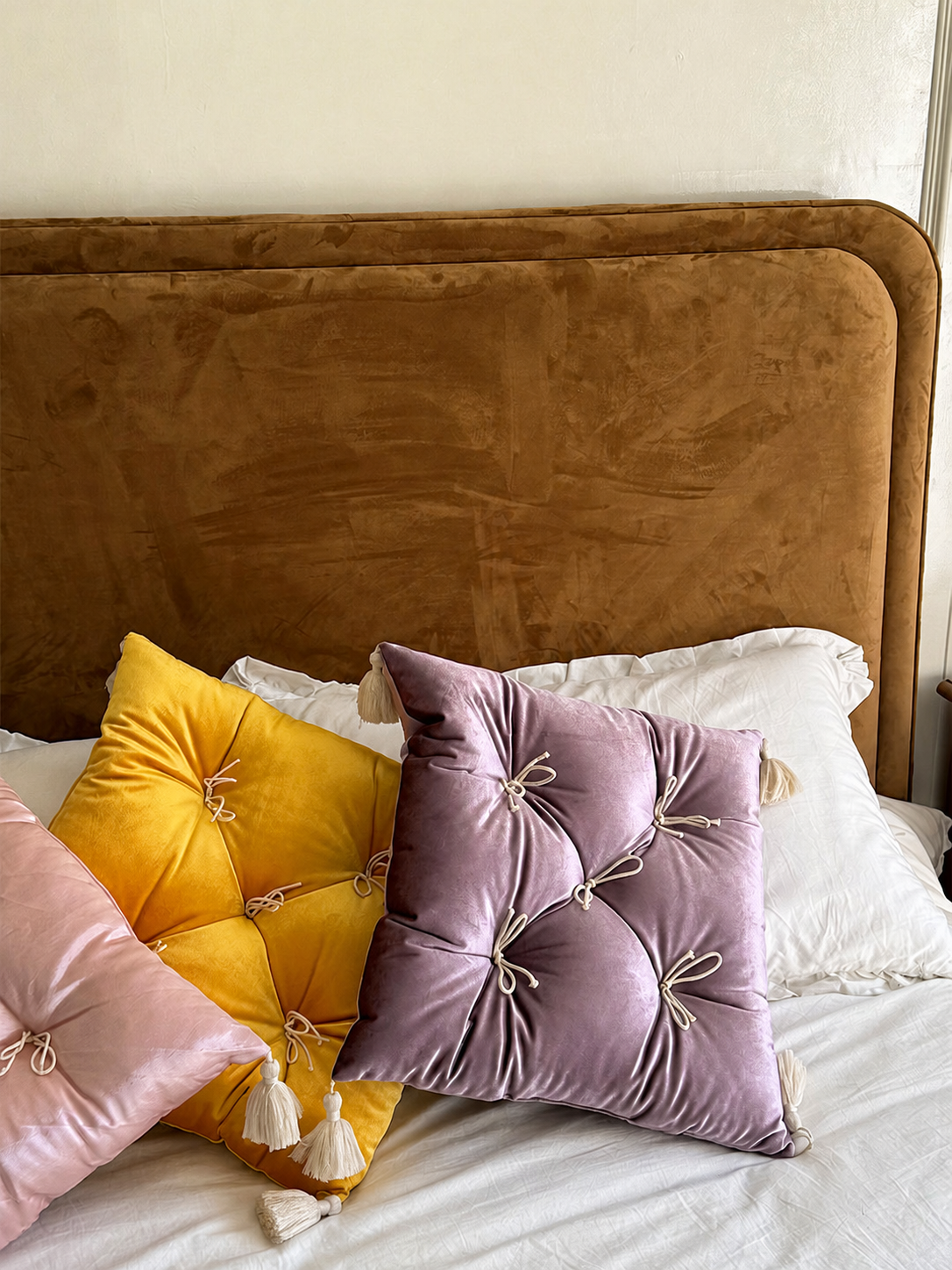 Yellow, purple, and rouge Mariette velvet tufted tassel throw pillows styled on a bed.