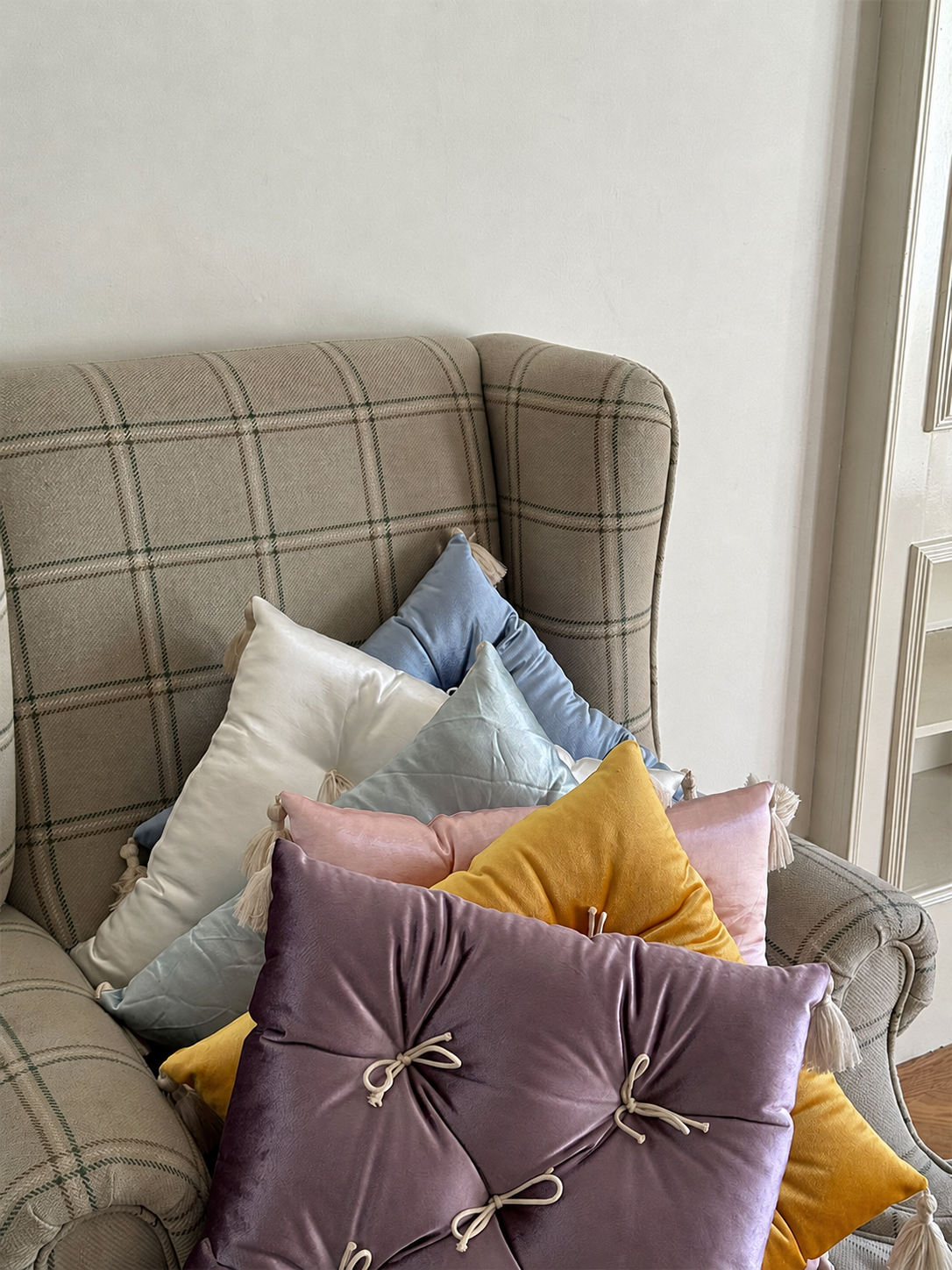 Assorted Mariette velvet tufted tassel throw pillows styled on a plaid armchair.