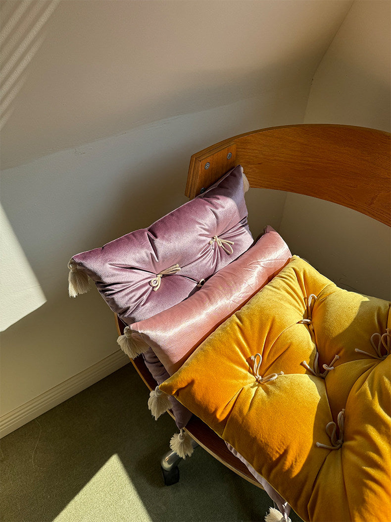 Purple, rouge, and yellow Mariette velvet tufted tassel throw pillows styled on a sunlit chair.