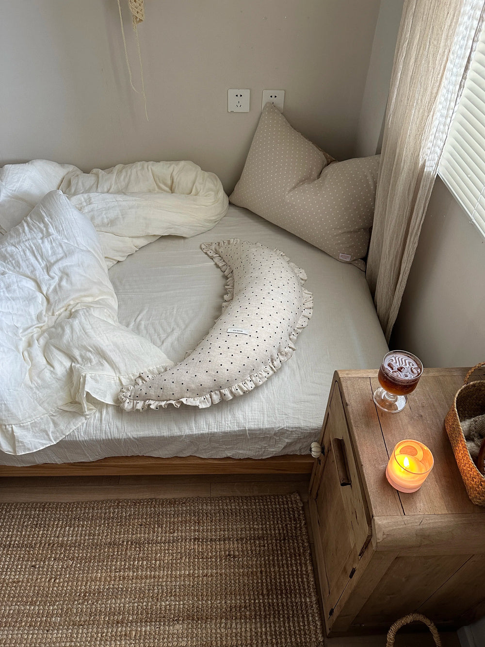 Polka dot linen moon body pillow cushion styled on a cozy bed beside a wooden nightstand.