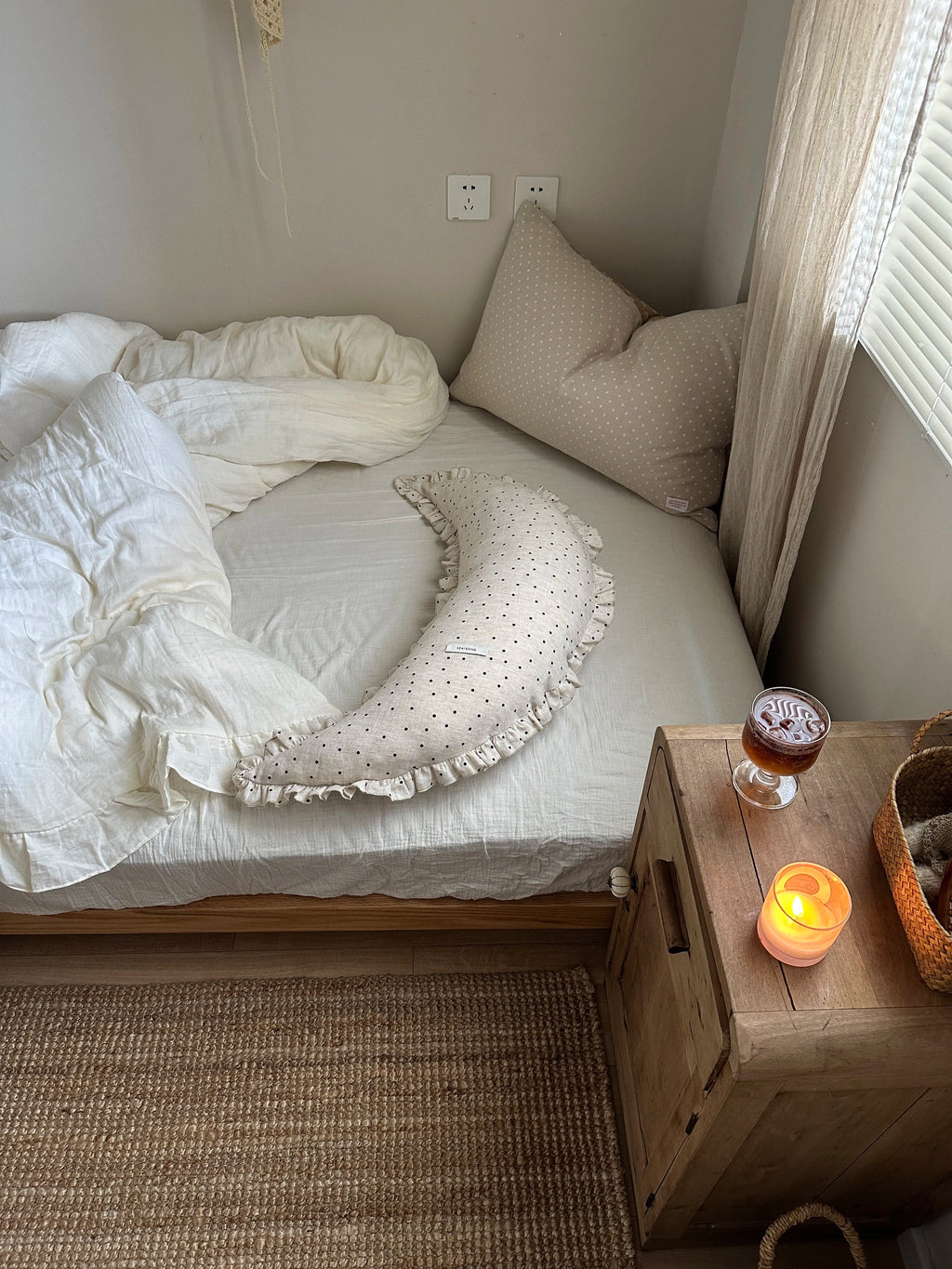 Polka dot linen moon body pillow cushion styled on a cozy bed beside a wooden nightstand.