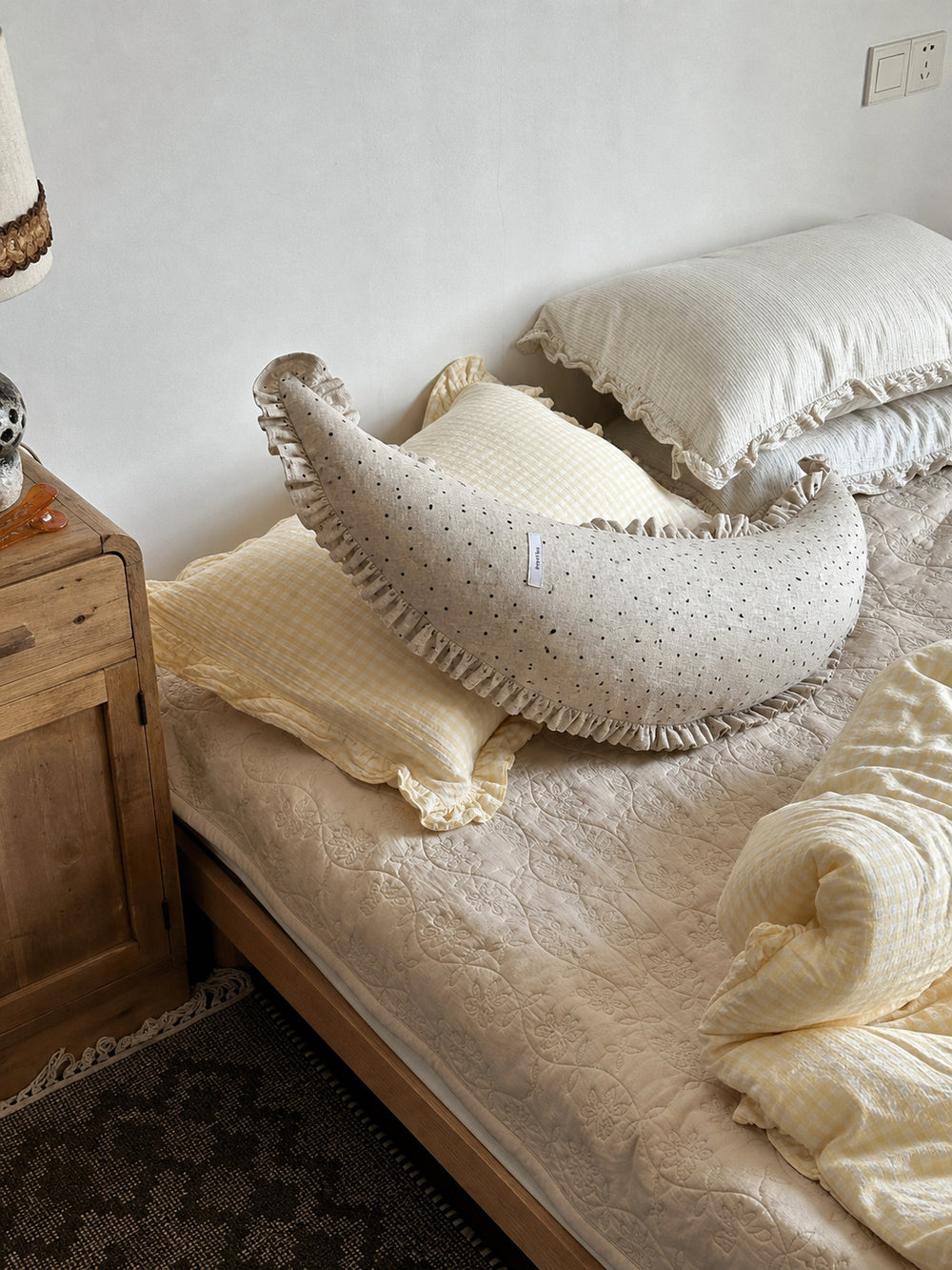 Polka dot linen moon body pillow cushion styled across yellow gingham bedding in a bedroom scene.