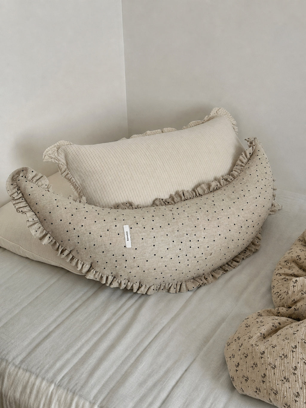 Polka dot linen moon body pillow cushion styled against a cream pillow in a corner bed scene.