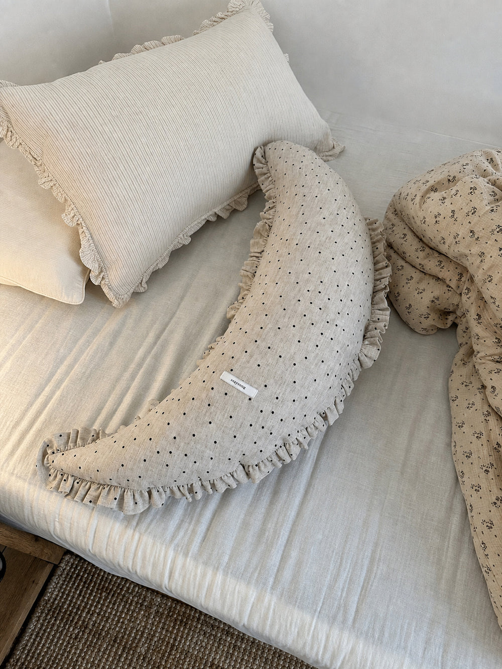 Polka dot linen moon body pillow cushion styled on cream bedding with floral bedding nearby.