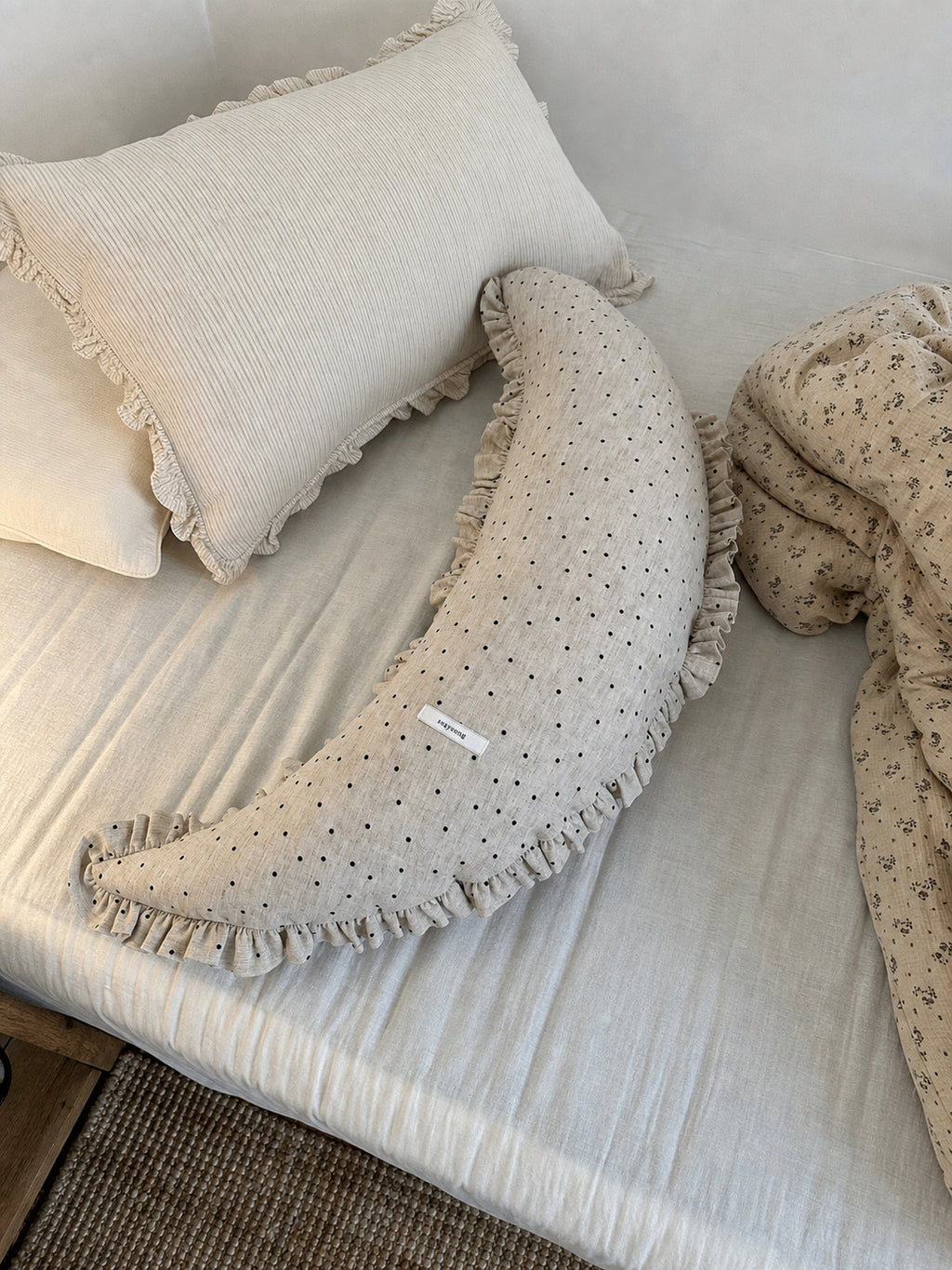 Polka dot linen moon body pillow cushion styled on cream bedding with floral bedding nearby.