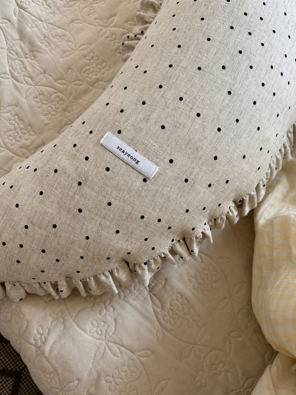 Close-up detail of the polka dot linen moon body pillow cushion fabric, sewn label, and ruffled trim.