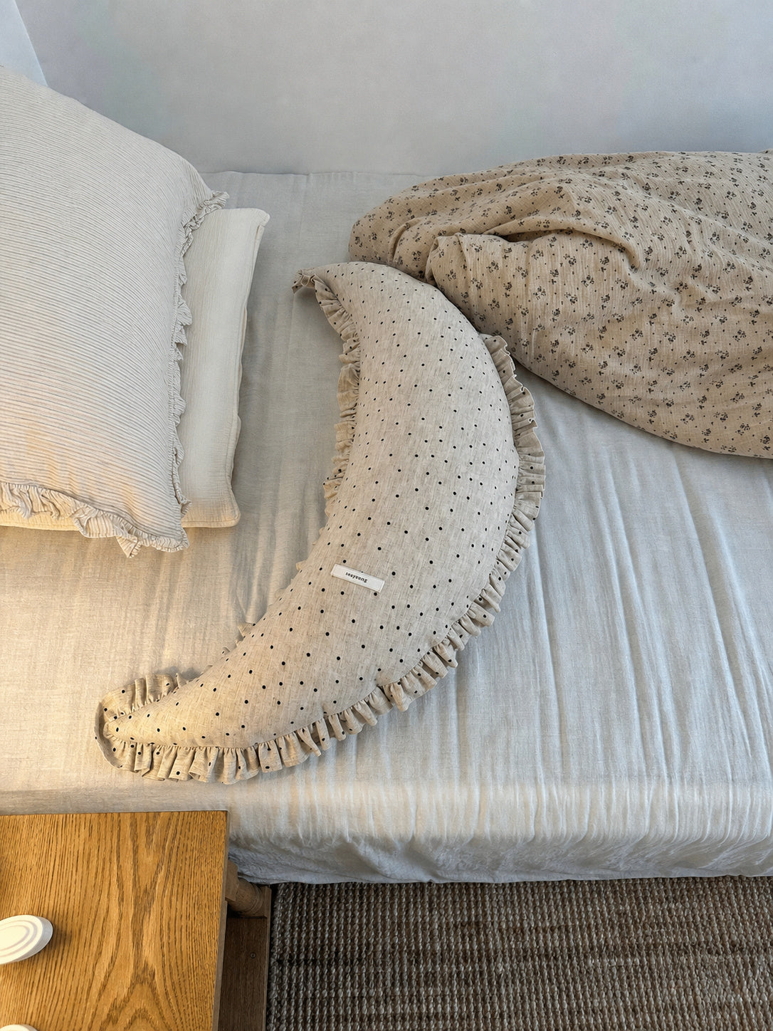 Polka dot linen moon body pillow cushion on white bedding with floral bedding in the background.