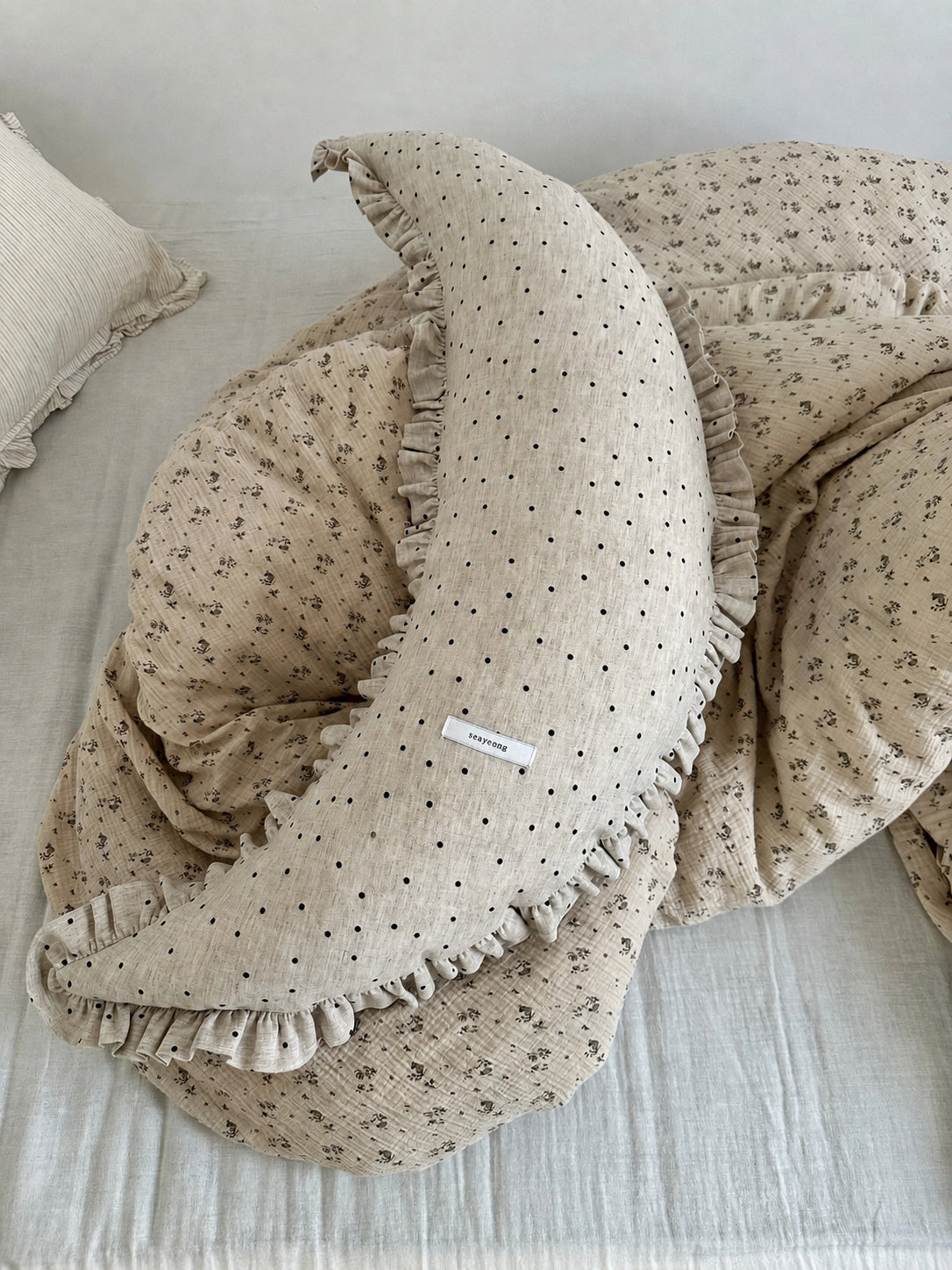 Polka dot linen moon body pillow cushion styled on floral quilted bedding.