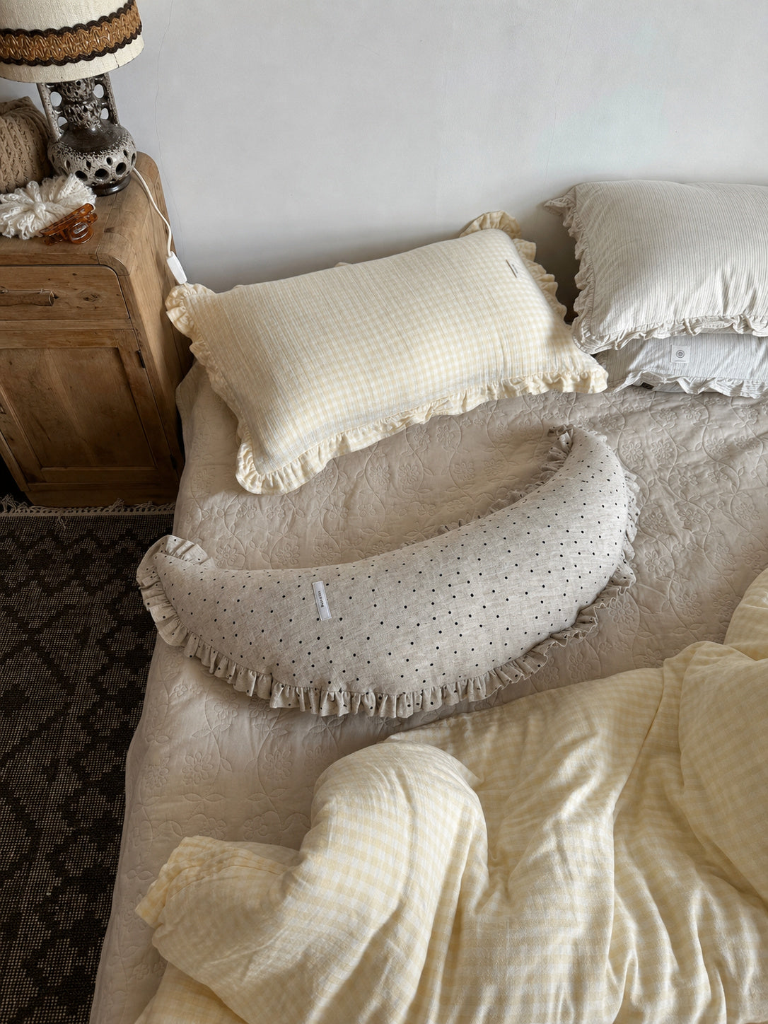 Polka dot linen moon body pillow cushion styled on a bed beside a wooden nightstand and lamp.