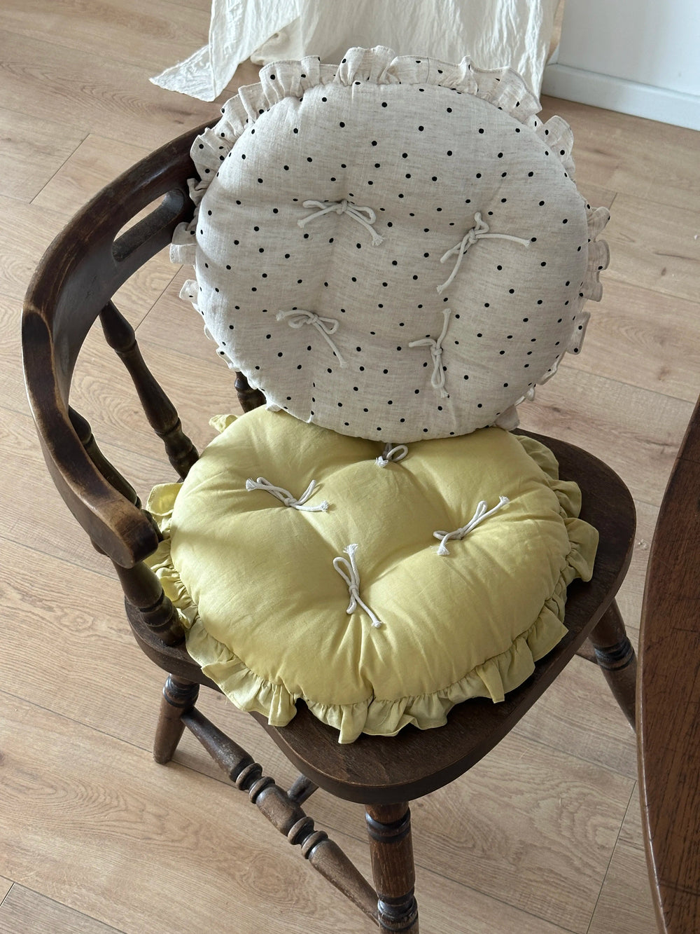 Cream polka dot and soft yellow round chair cushions with bow ties and ruffled edges styled on a wooden chair.