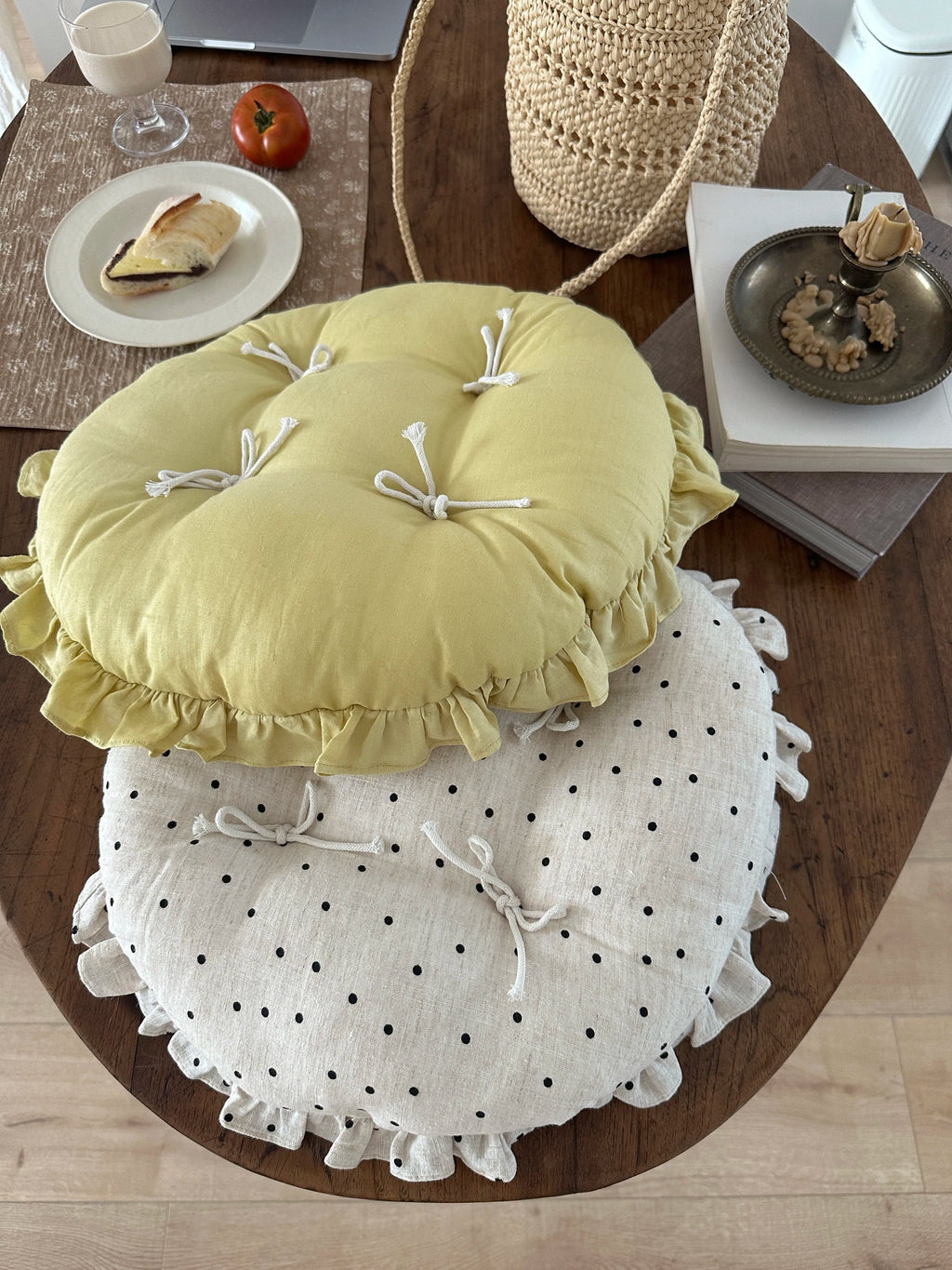 Soft yellow and cream polka dot round chair cushions with bow ties and ruffled edges viewed from above on a wooden table.