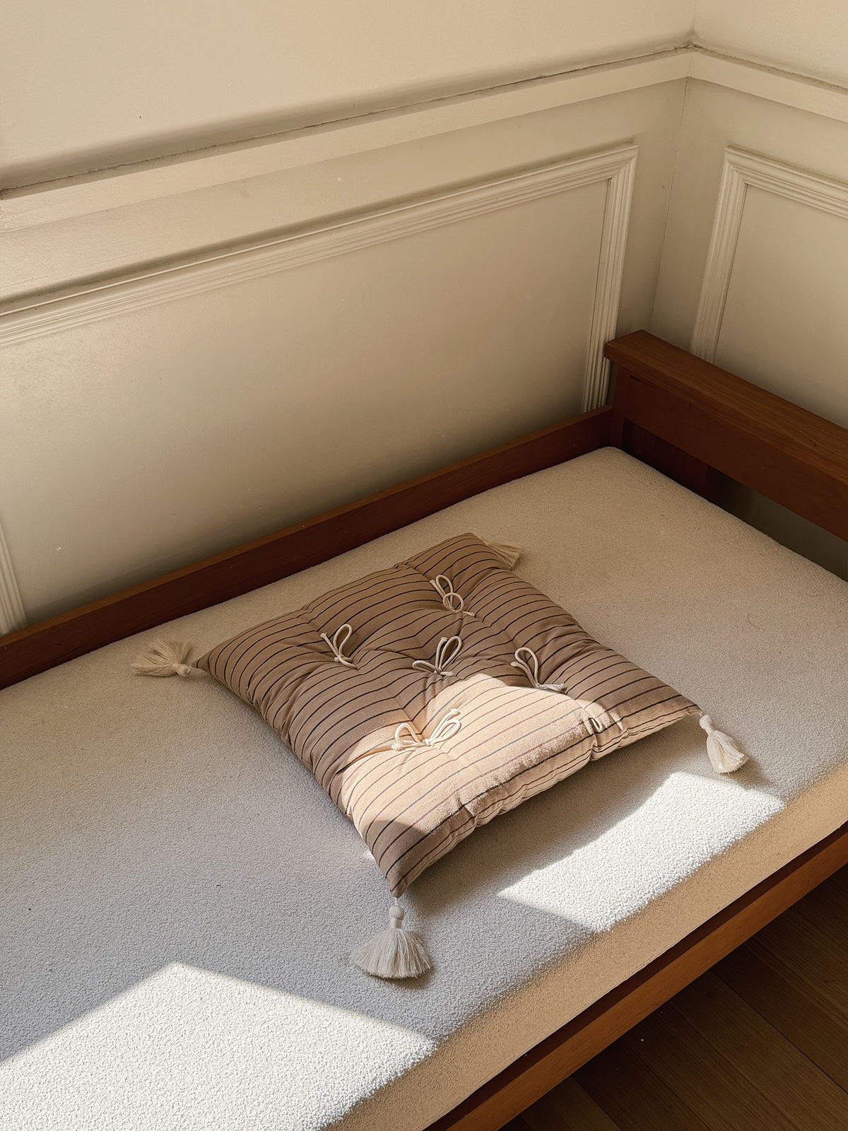 Beige Stripes Mariette tufted tassel throw pillow displayed on a sunlit bench.
