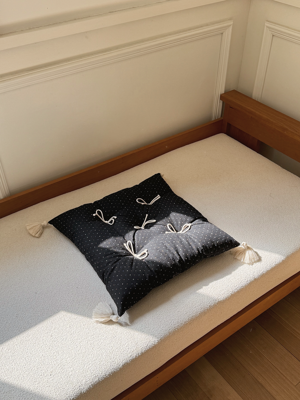 Black Polka Dot Mariette tufted tassel throw pillow displayed on a sunlit bench.