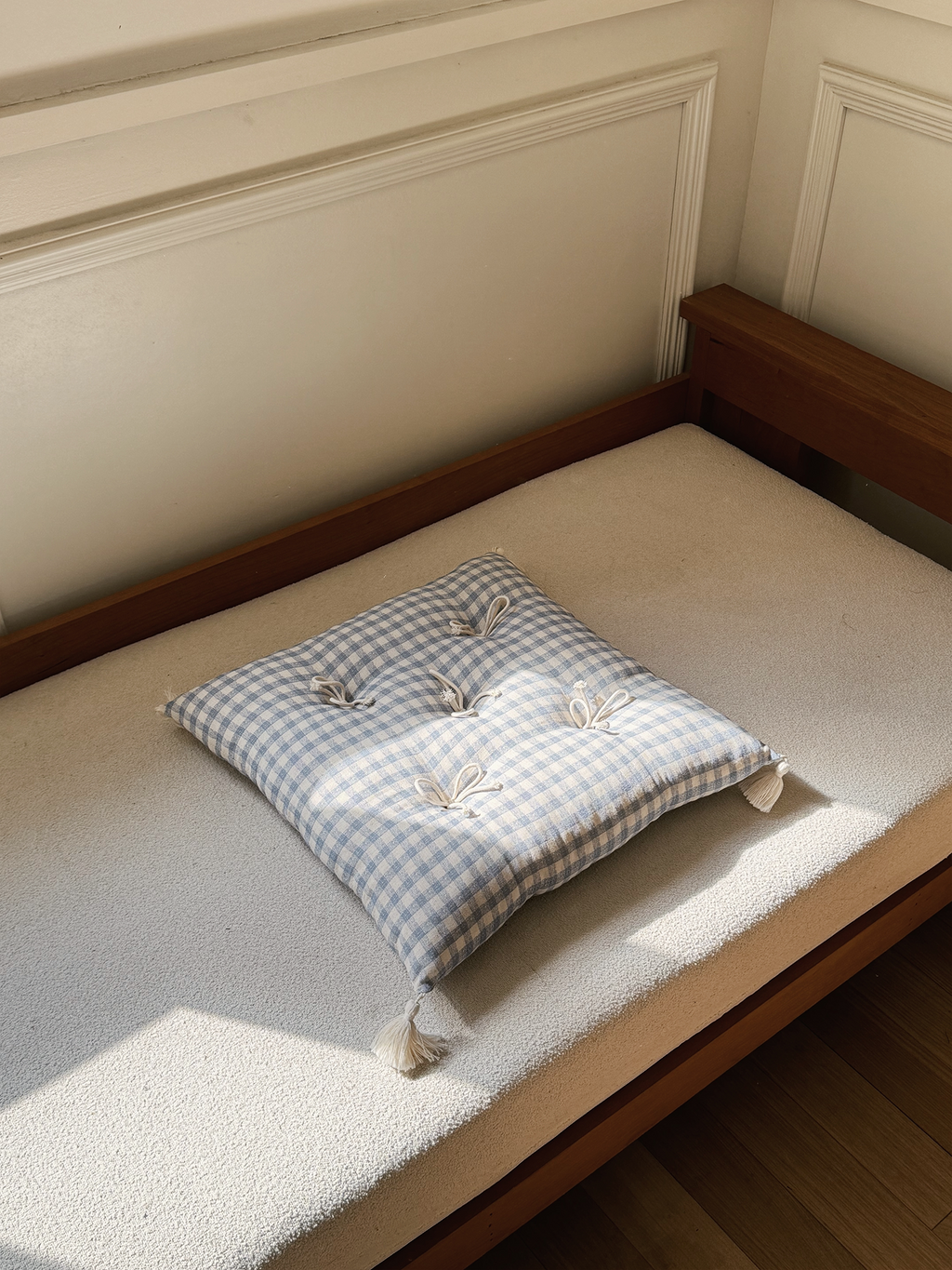 Cream and Blue Plaid Mariette tufted tassel throw pillow displayed on a sunlit bench.