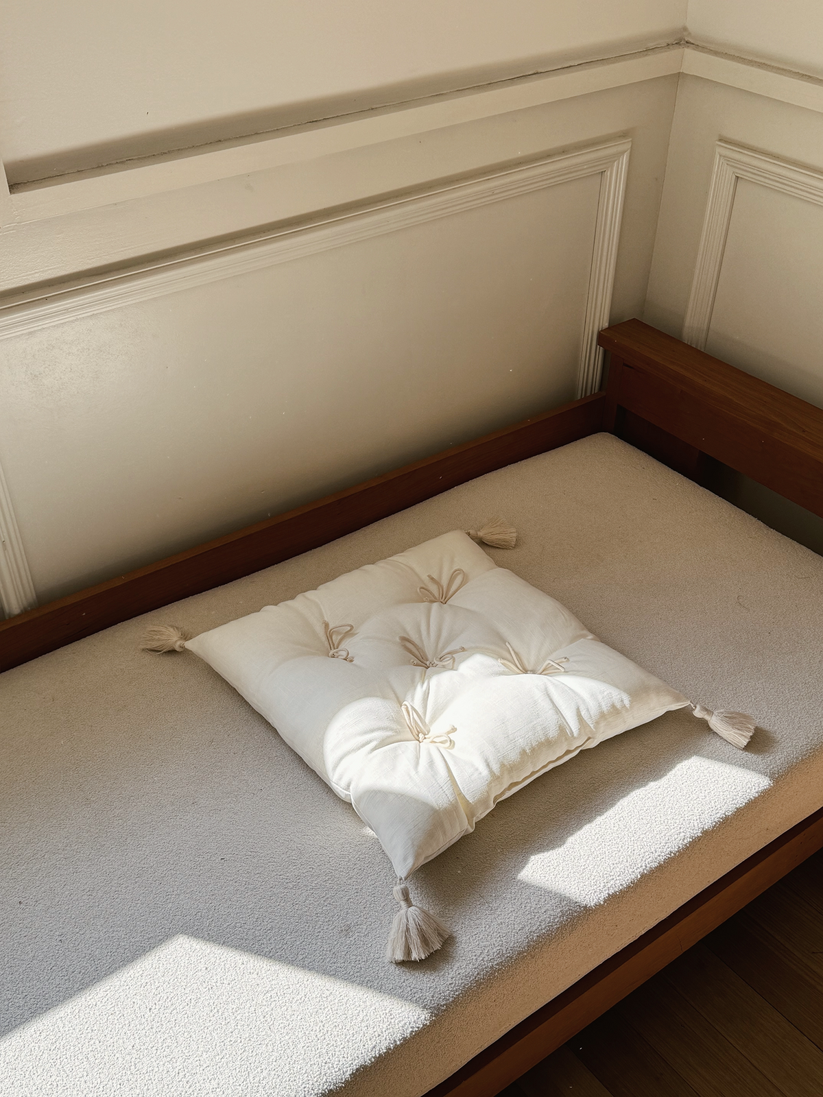Ivory Cotton Mariette tufted tassel throw pillow displayed on a sunlit bench.