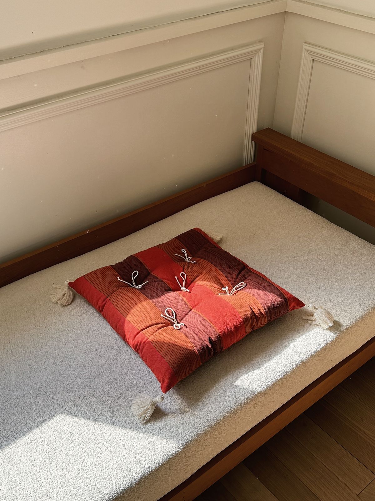 Vintage Sunset Red Mariette tufted tassel throw pillow displayed on a sunlit bench.
