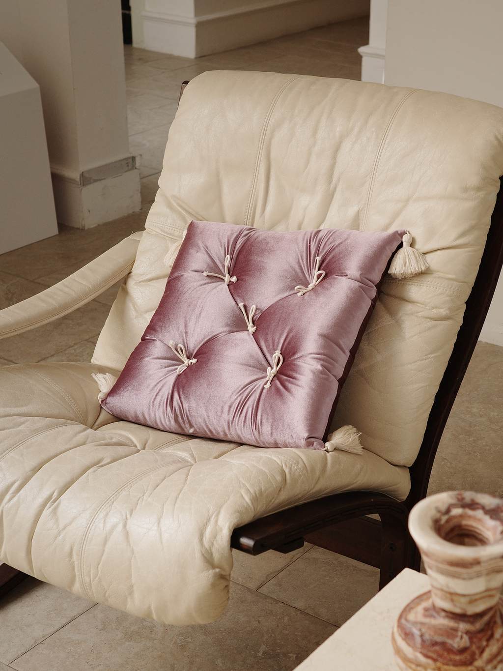 Purple Velvet Léonie tufted tassel throw pillow styled on a cream lounge chair.