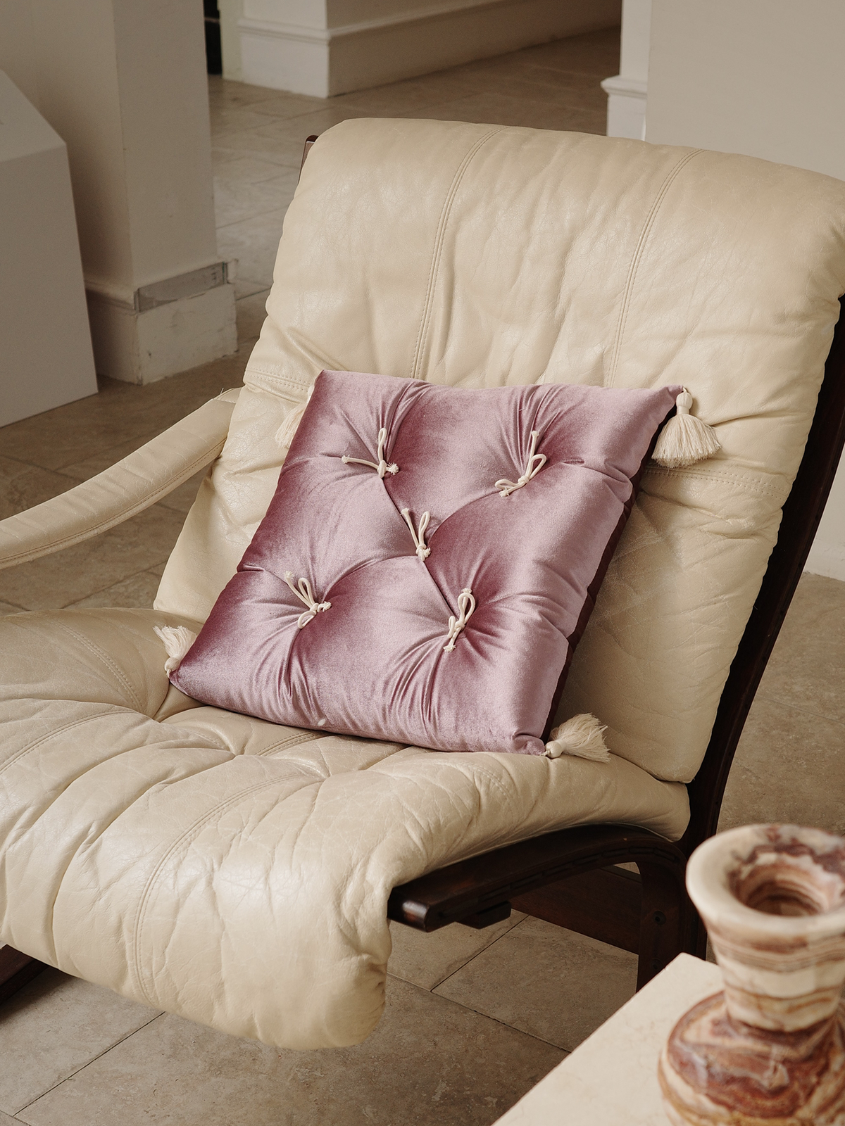 Purple Velvet Léonie tufted tassel throw pillow styled on a cream lounge chair.