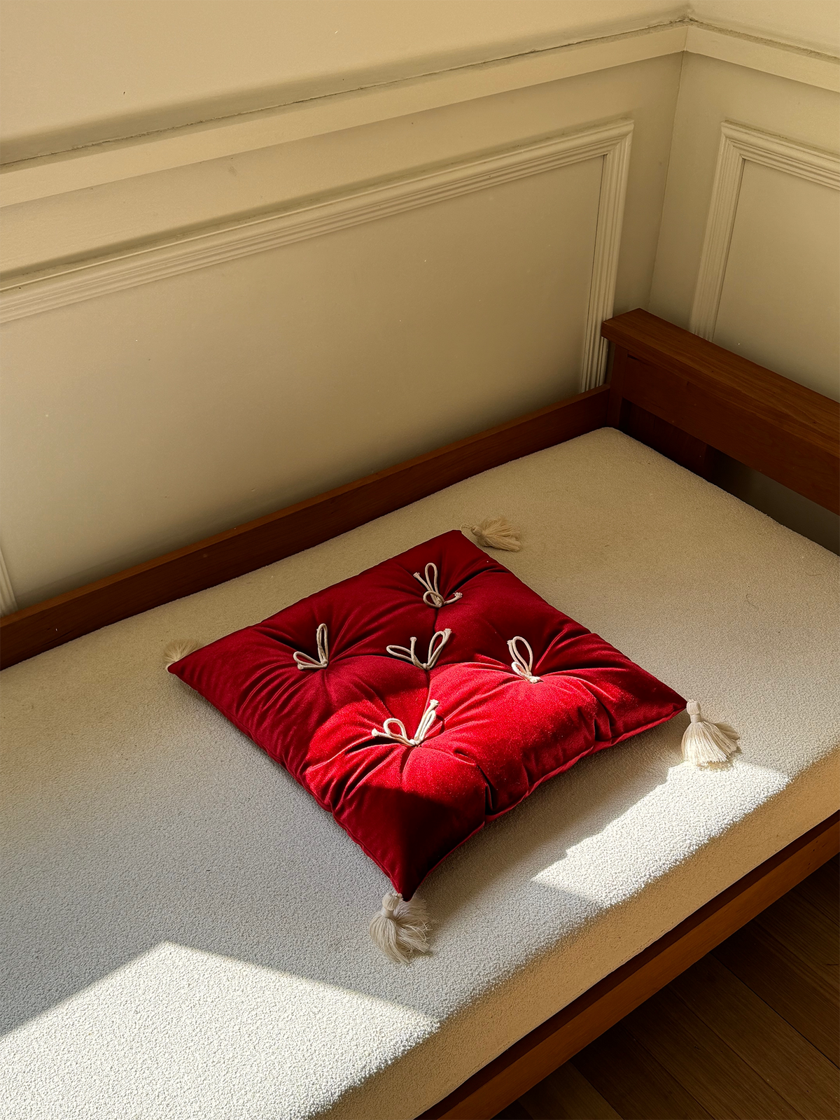 Rouge Velvet Léonie tufted tassel throw pillow displayed on a sunlit bench.