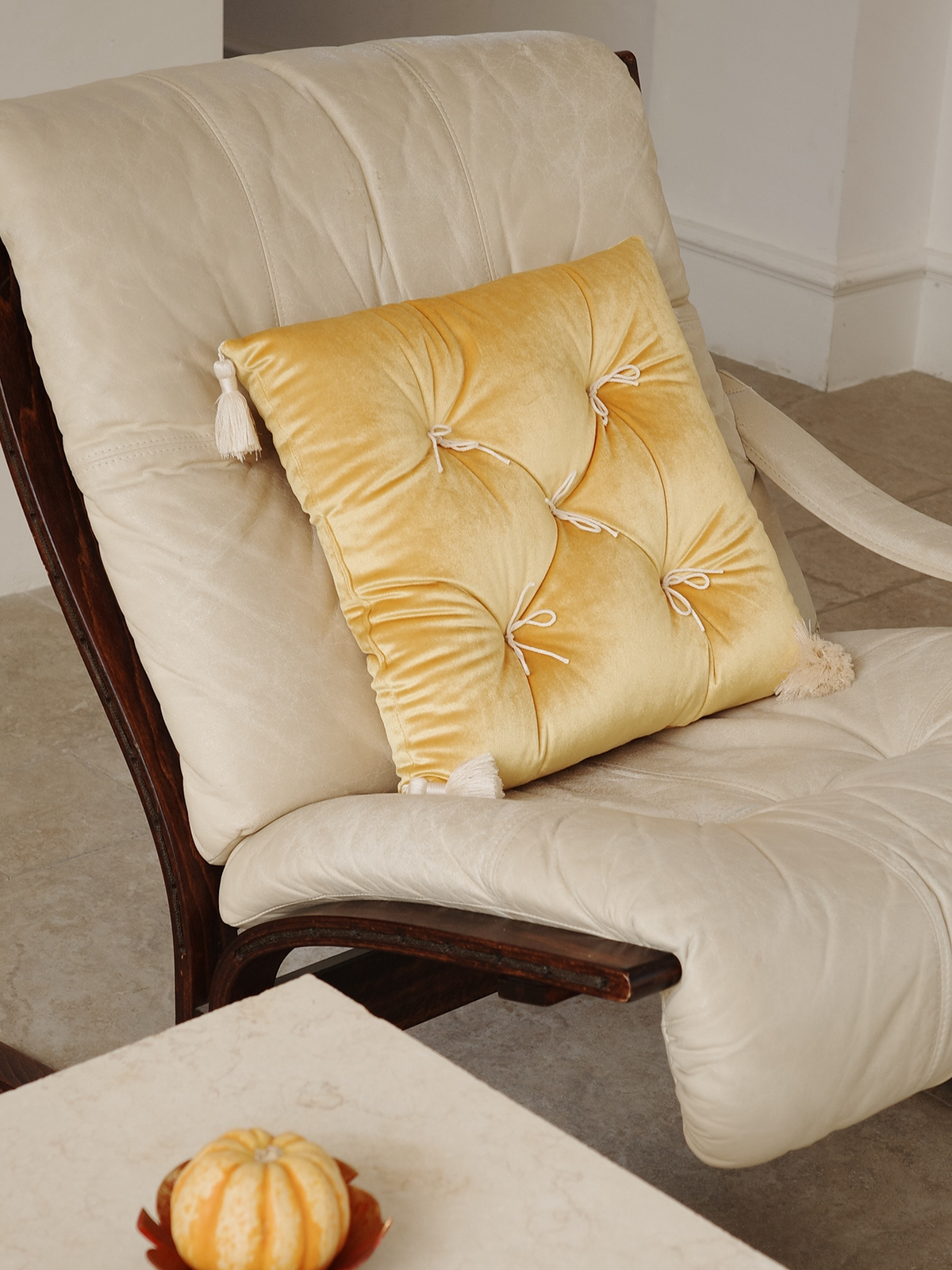 Yellow Velvet Léonie tufted tassel throw pillow styled on a cream lounge chair.
