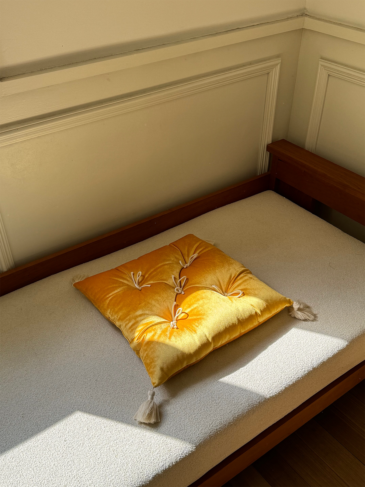 Yellow Velvet Léonie tufted tassel throw pillow displayed on a sunlit bench.